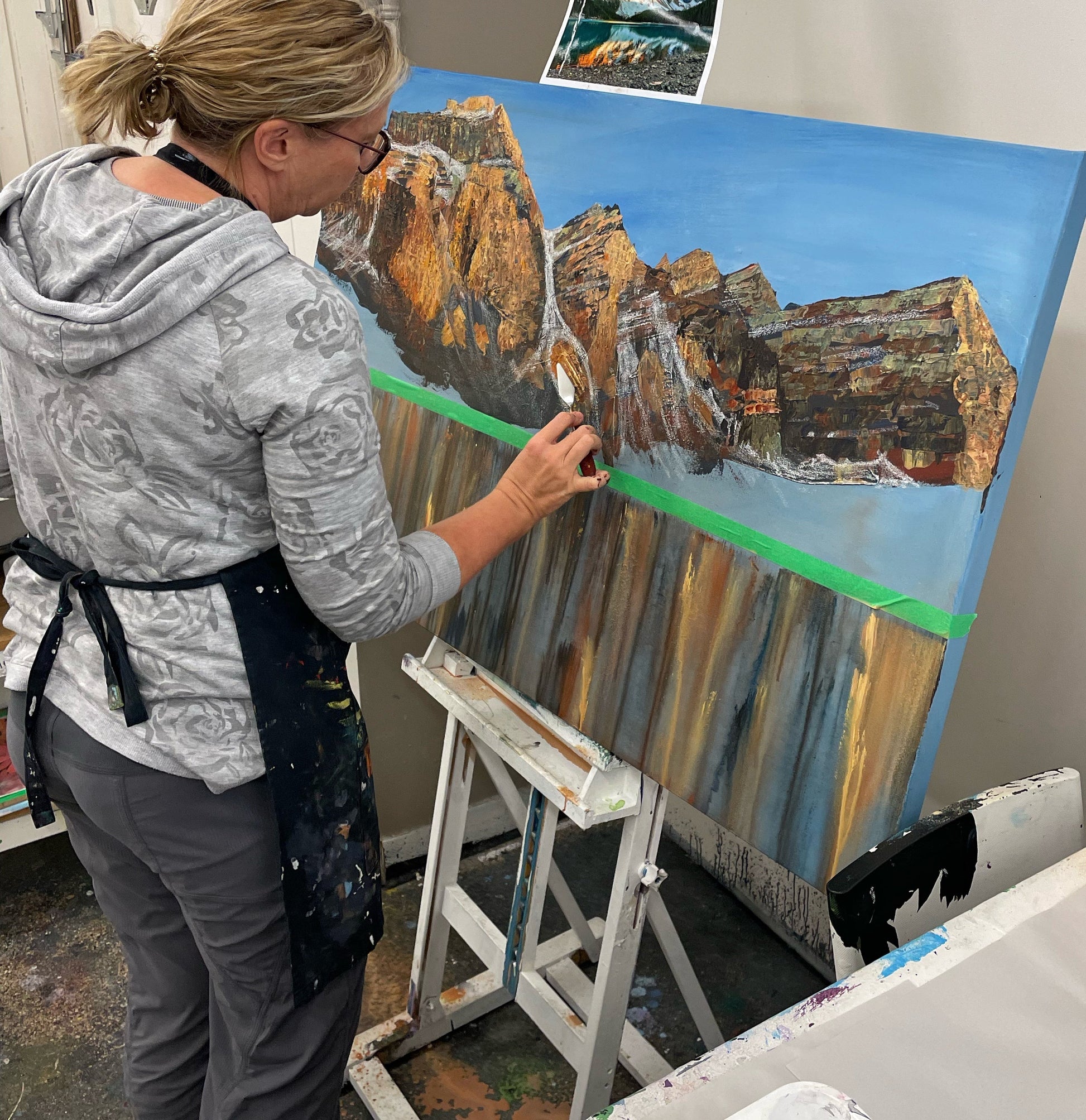 Teresa Grasby demonstrating palette knife technique on a large mountain canvas at her NW Calgary studio
