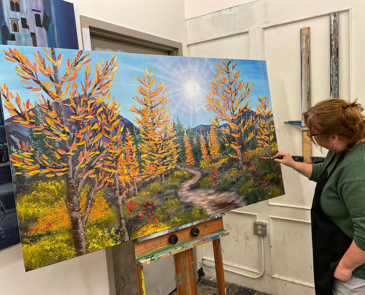 Teresa Grasby holding a large-format golden larch treescape painting at her NW Calgary studio