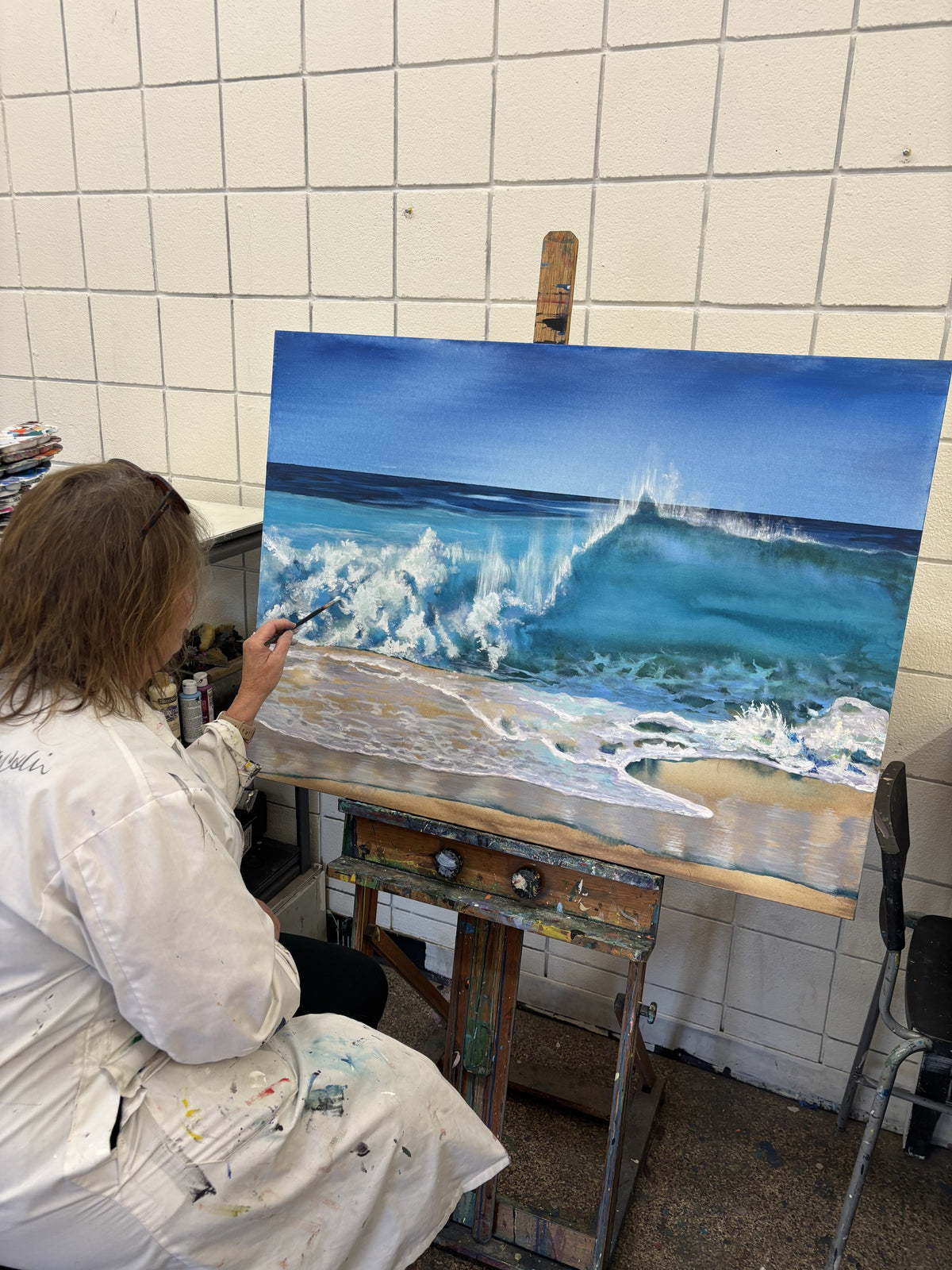 Student painting a turquoise breaking wave at the easel in the Water & Waves workshop, Grasby Art Studio, NW Calgary